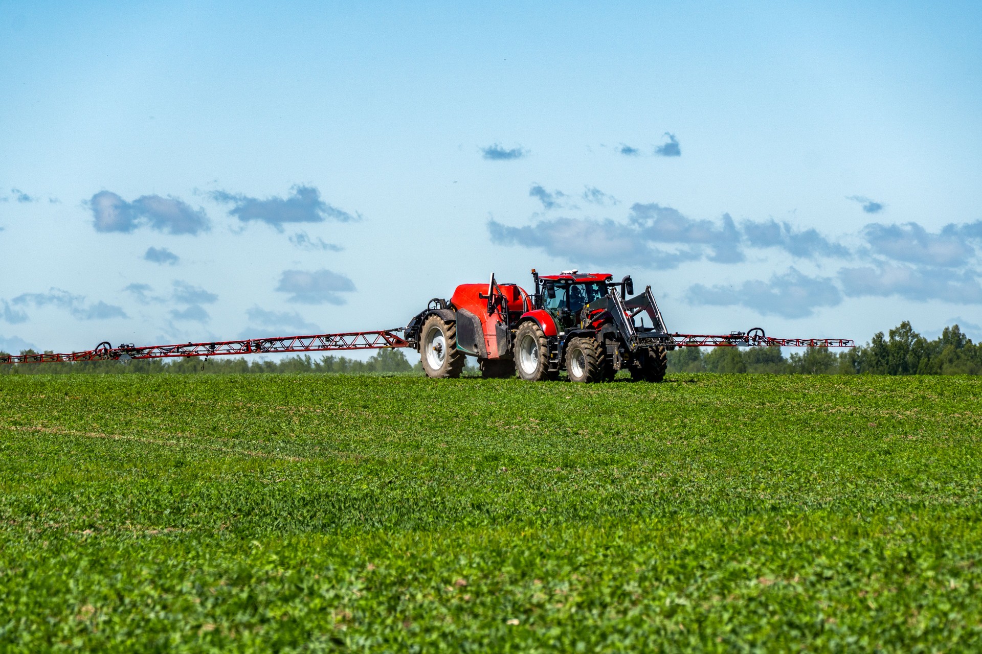 Modern Red Tractor with Sprayer Working in Green Field on Sunny Day  Precision Agriculture and Sustainable Farming Equipment in Action